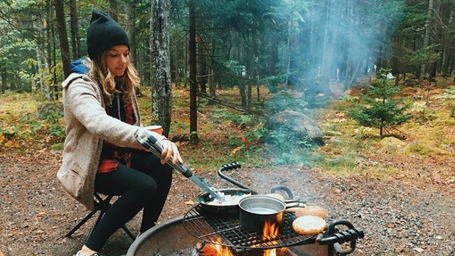 Woman cooks food in fire ring