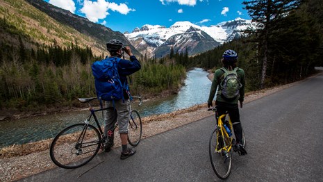 Two bicyclists standing with bicycles looking at a mountain.