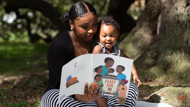 a mother reads to her baby underneath a tree