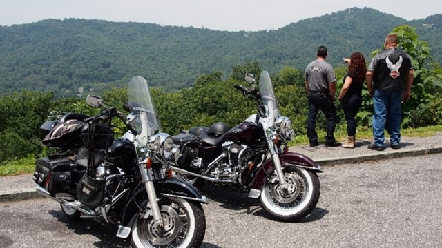 Three people standing next to two motorcycles looking at an overlook at a designated pull off spot.