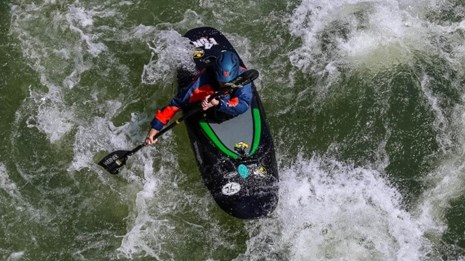 kayaker in white and green waters of river rapid as seen from above on a bridge