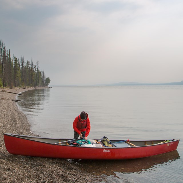 Woman wearing a life jacket stands beside canoe