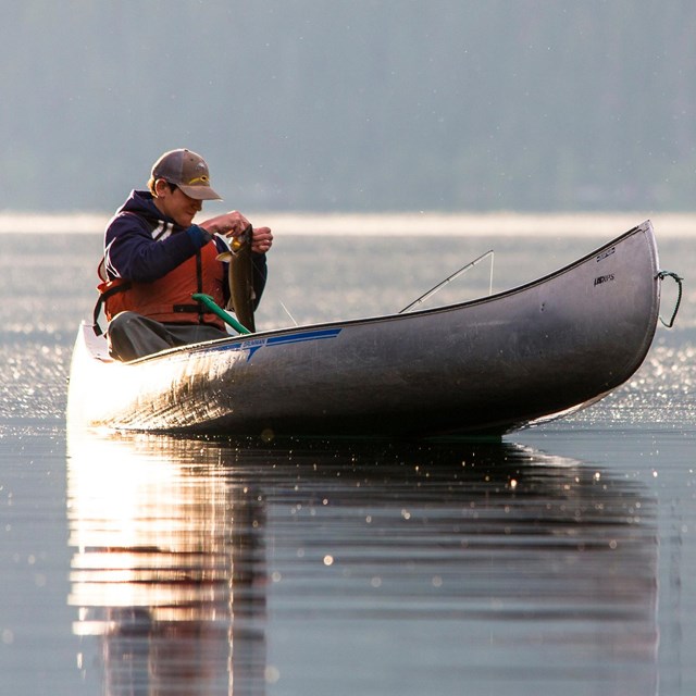 Fisherman wearing a life jacket unhooking fish from canoe