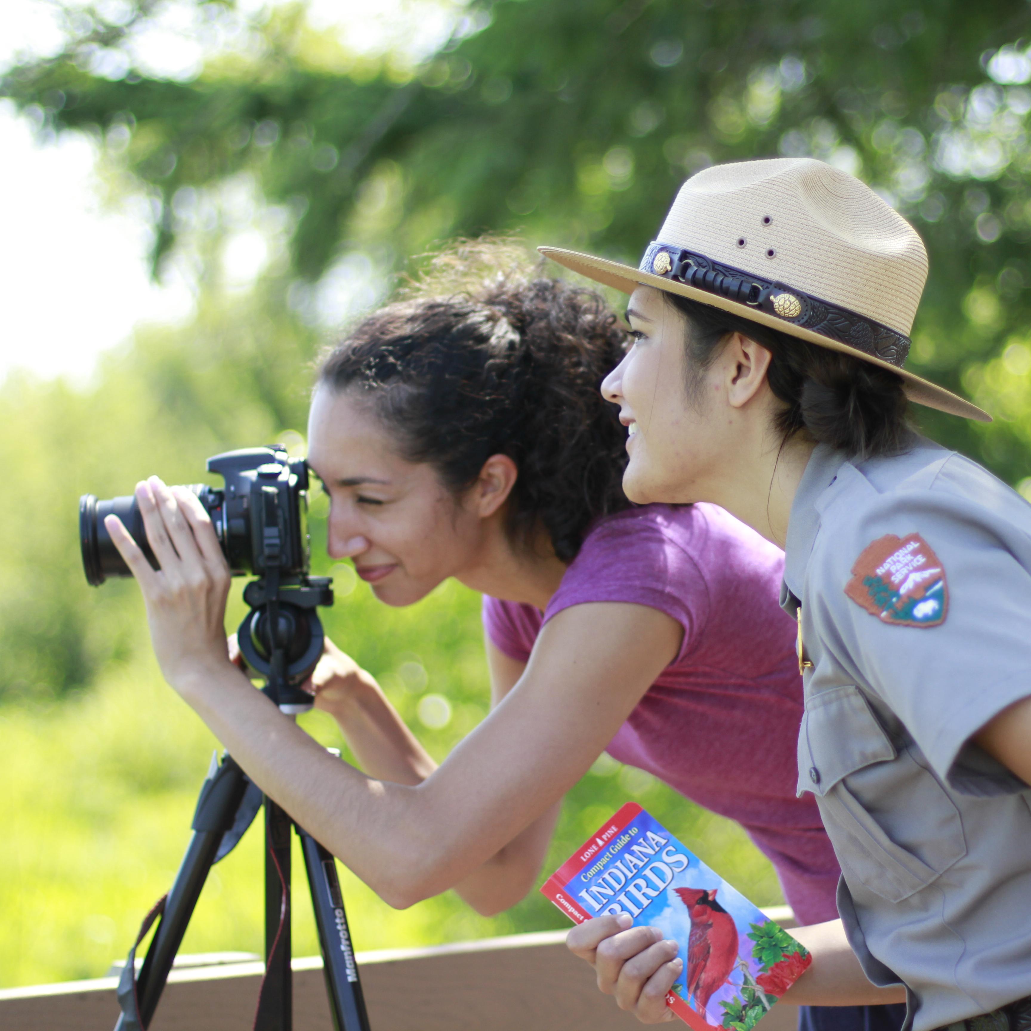 Park ranger standing beside visitor looking through camera
