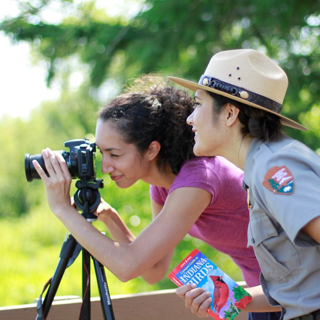 Park ranger standing beside visitor looking through camera