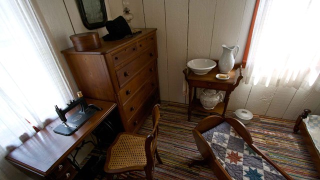 A small room is furnish with an antique bureau, sewing machine, and cradle.