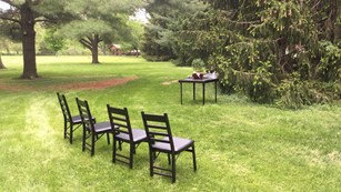 Four chairs and table set a park lawn await a wedding ceremony.