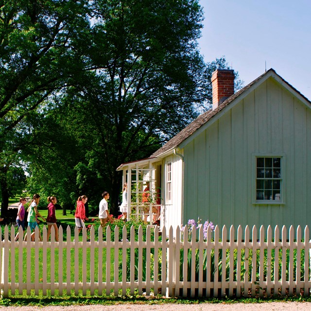 Schoolchildren enter single file into a historic white cottage.