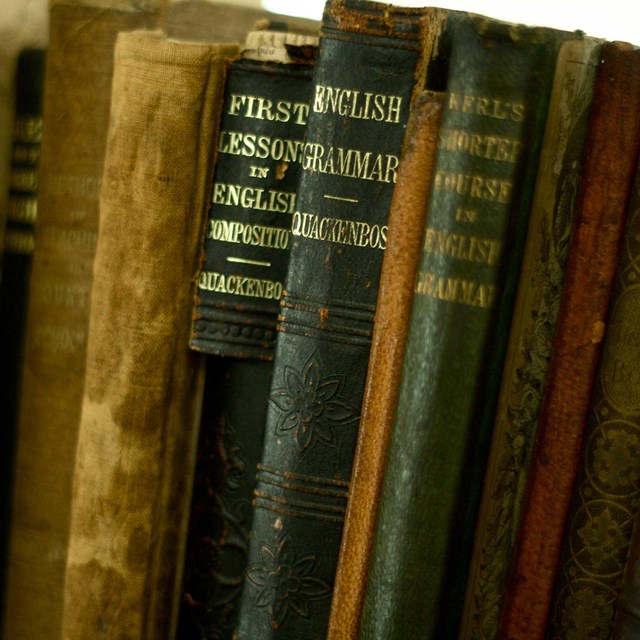 Antique bound textbooks and readers line a shelf in a historic school.