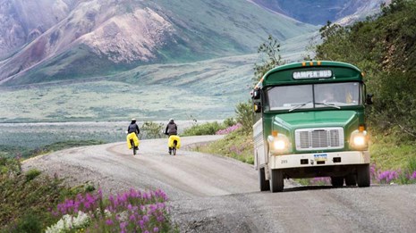 green bus past two bikers headed towards mountains