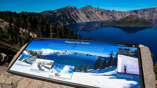 Wayside sign in front of blue lake and crater ridge line 