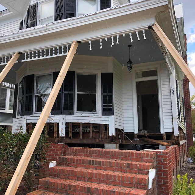 White frame home with porch roof supported by temporary shoring.