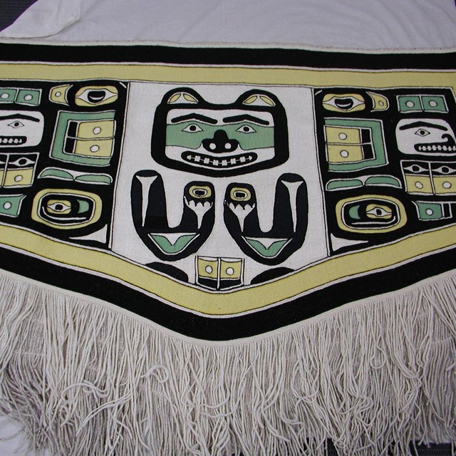 Fringed white robe with bear motif in green, black, and yellow