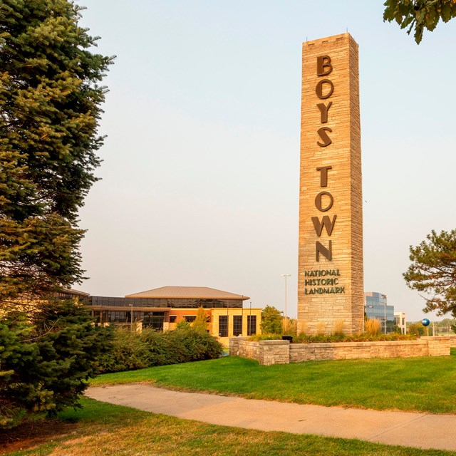 Tall stone bell carillon at sunset; outdoors with path and trees foreground