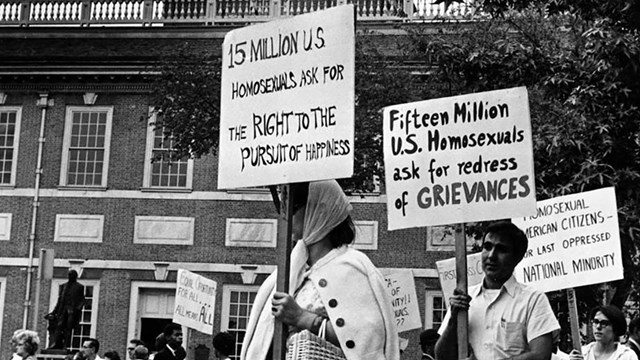 People carry signs as part of a gay rights demonstration with buildings in the background