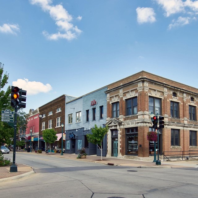 A view down a small town street corner shows several two story buildings and storefronts.