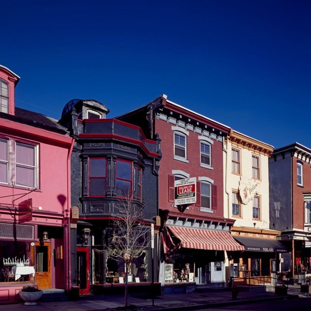 Several adjoined three-story buildings with awnings and storefronts on the street level. 