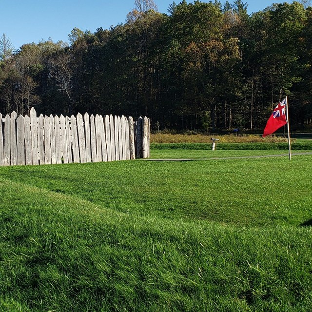 A grassy field with military earthworks leading to a log fortification