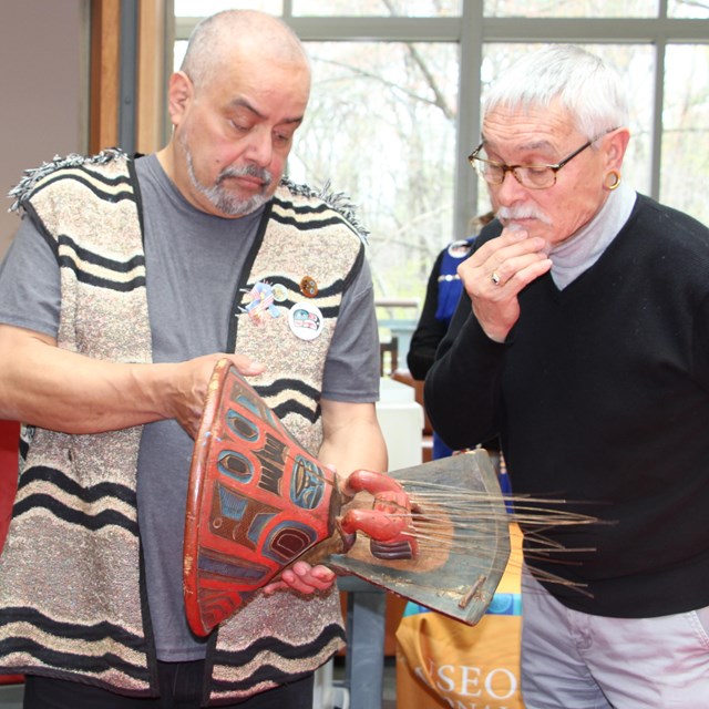 Three men look at a hand carved wooden object.