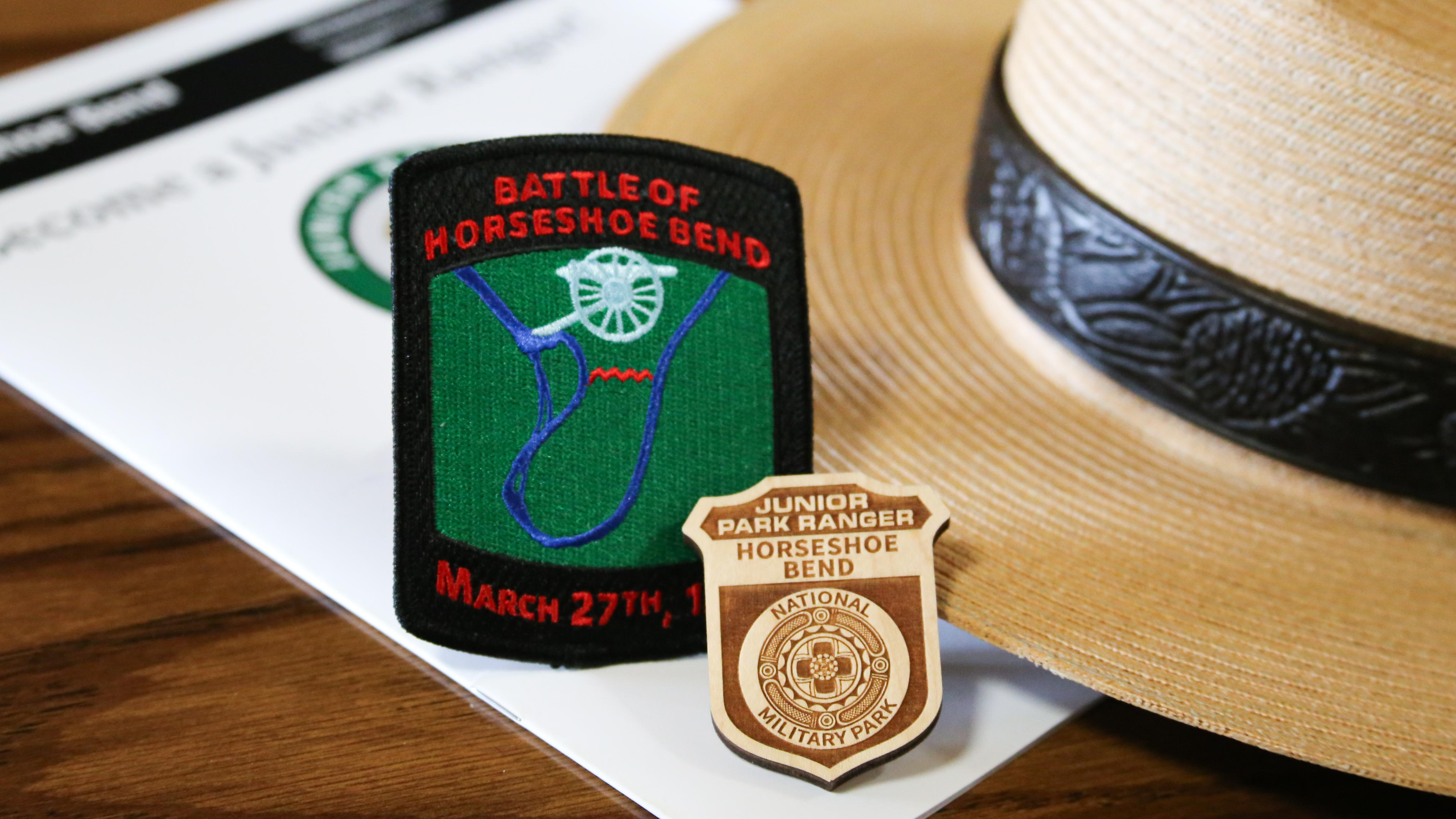 A Junior Ranger badge and iron-on patch lean on a ranger flat-hat. 