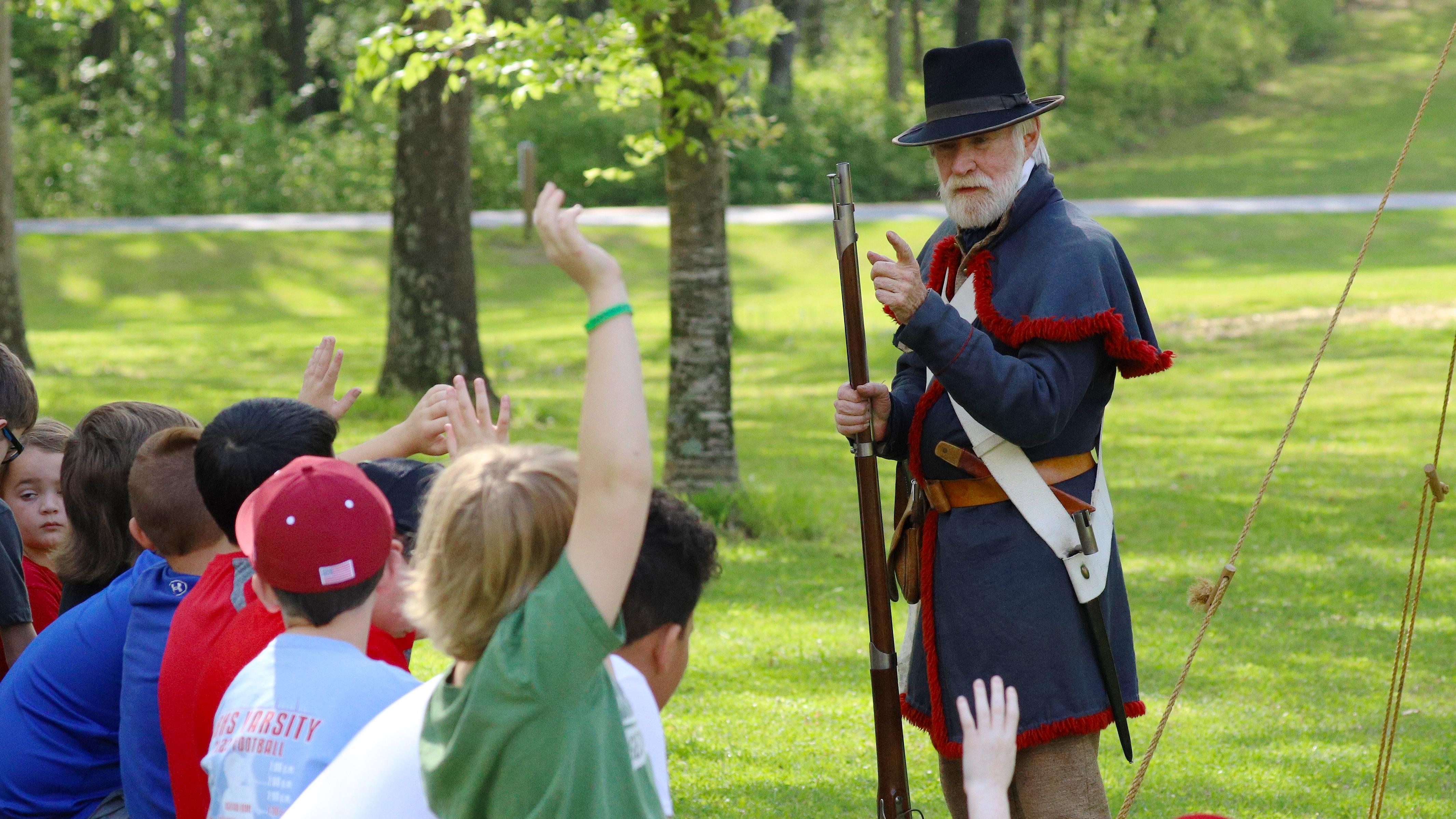 living history demonstrator dressed in 19th century military outfit is talking to a group of kids. 