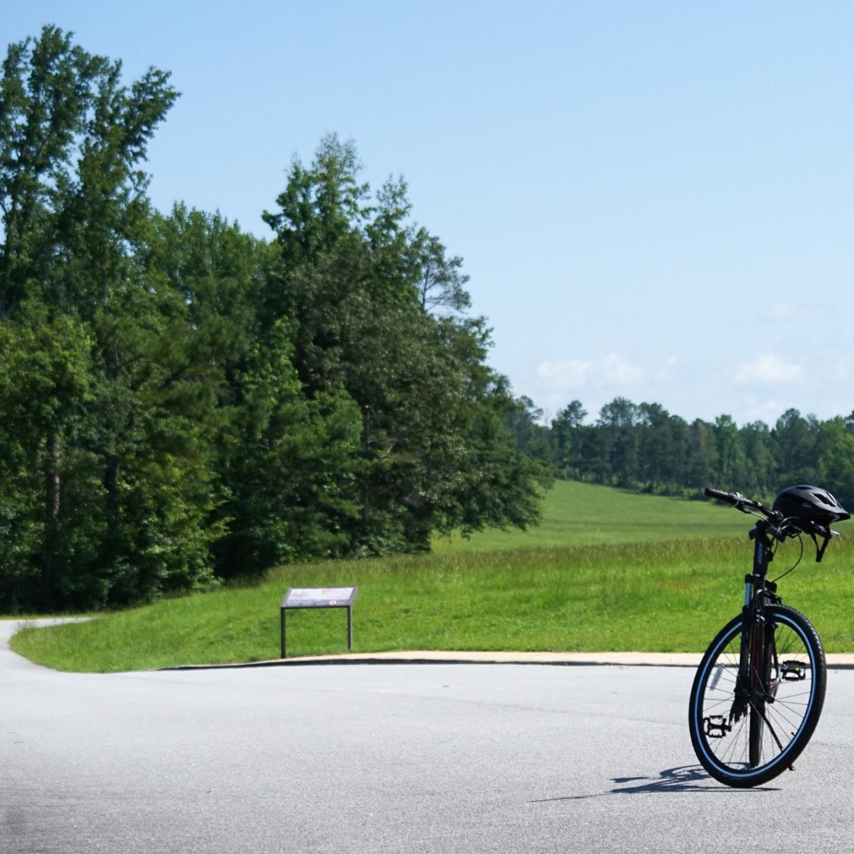 Image displays a bicycle with a helmet placed on a paved road with grass and trees in the background