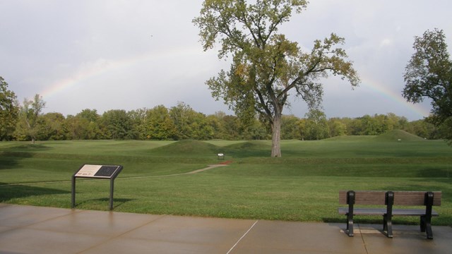 A multi-colored rainbow arches about a field of grass-covered earthen mounds