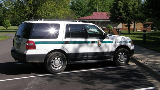 A white truck with green stripe and police lights on top sits in a parking lot