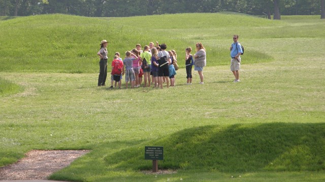 Park visitors in a grassy area talking with a ranger in a flat hat