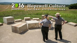 A park ranger points out towards a field with another standing alongside, behind large marble stones