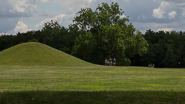 Park visitors in a grassy area walking around large, green, grass-covered mounds