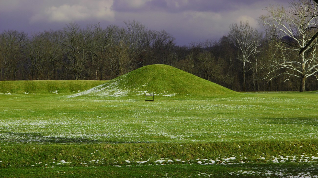 A large grass-covered mound under a dark grey sky