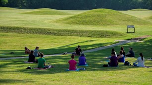 Several people sitting on the grass in front of mounds