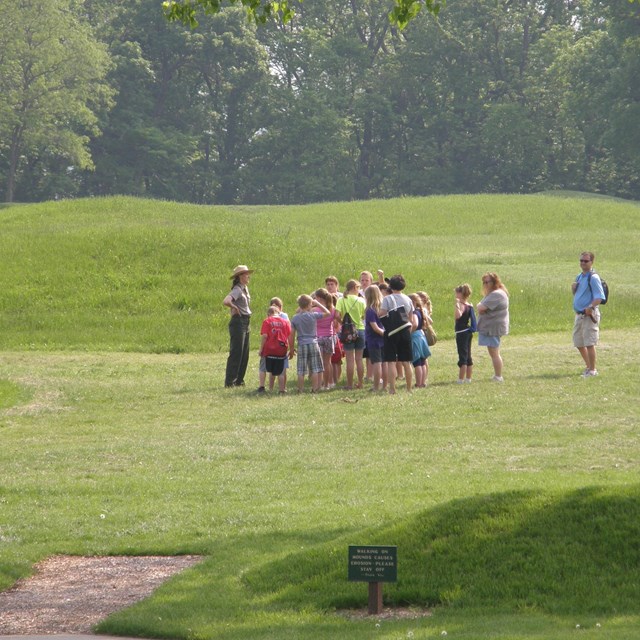 A group of visitors listen to a ranger as they stand near mounds