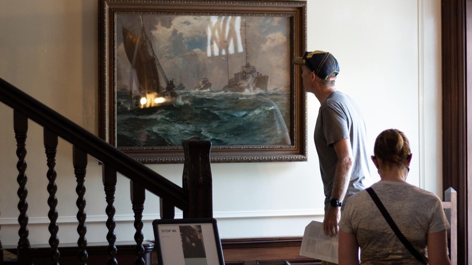 A man on a stair landing studies a painting hanging on the wall.