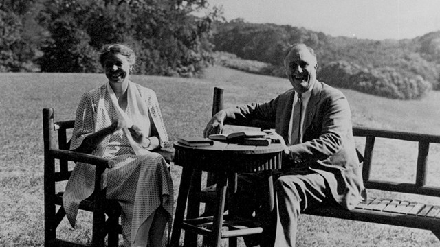A happy man and woman seated on a lawn with river in the distance.