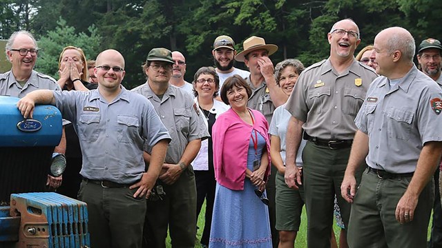 A group of park rangers gathered on a lawn next to a tractor.