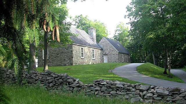 A stone house on a gentle hilltop clearing surrounded by woods.