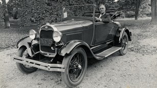 A man in a suit behind the wheel of an open air car.