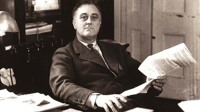 A man wearing a suit (Franklin Roosevelt) seated behind a desk.