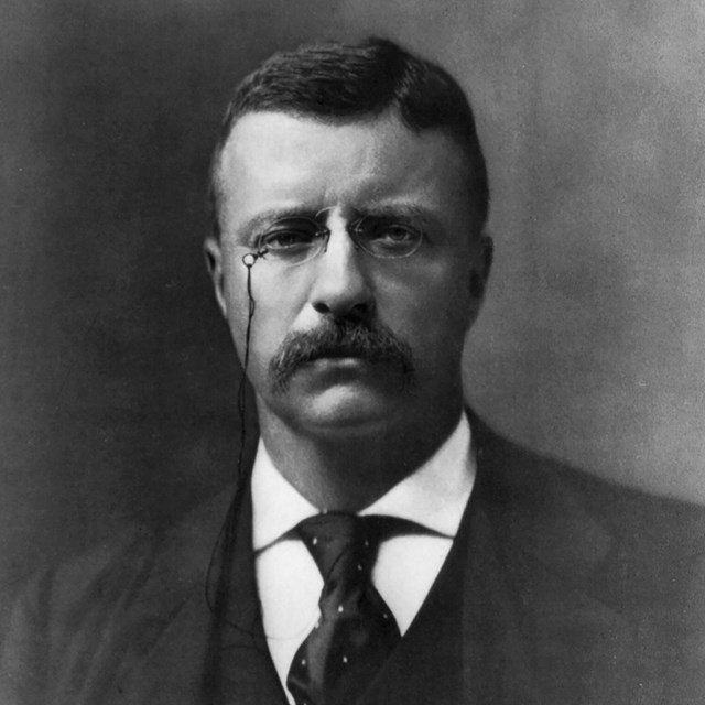 A man with eye glasses wearing a suit and tie.