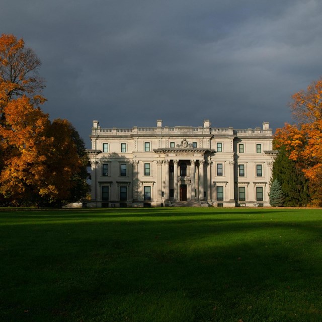 A stone mansion set amid a vast green lawn and autumn trees.