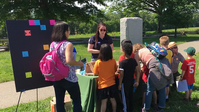 Staff and AmeriCorps intern engage with group of homeschoolers about iron making.
