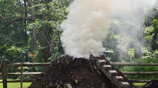 Wood pours out of earthen mound as wood burns to create charcoal.