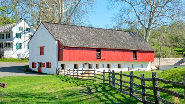 Red and white barn with fence in foreground. Ironmaster's Mansion is in view behind the barn. 