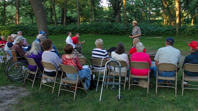 Outdoor seated visitors face inward toward a uniformed park ranger.