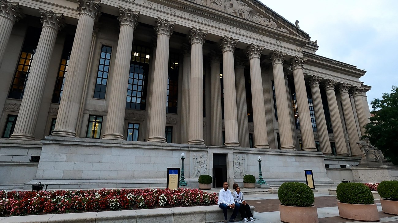 Black man sits with his daughter in front of the National Archives in Washington D.C.
