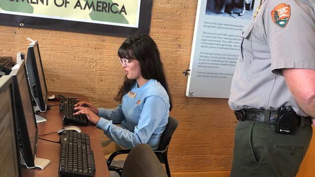 A researcher working on a computer with a ranger standing by and helping