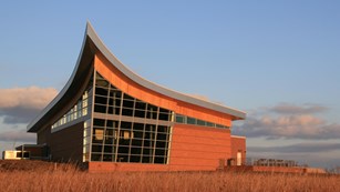 A plow-shaped building with lots of windows sits on the prairie.
