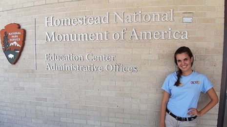 Person standing next to Homestead National Monument of America building sign